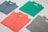 Four folded polo shirts in different colors are arranged symmetrically on a flat surface. The colors include blue, green, coral, and gray. Each shirt has a tag visible near the collar.