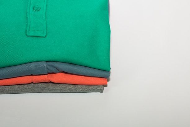 A neatly folded stack of vibrant polo t-shirts showcasing the neukite logo on a simple wooden table.