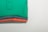 A stack of neatly folded polo shirts in four different colors, with the top shirt being green, followed by blue, coral, and grey. The shirts are arranged such that their collars and buttons are visible, indicating they are polo shirts. The background is a plain light color, highlighting the vividness of the folded shirts.