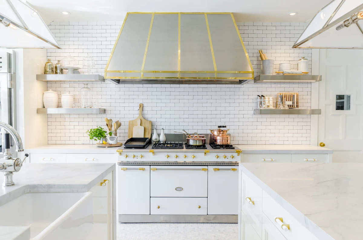 White and gold kitchen with a stainless range hood over the stove