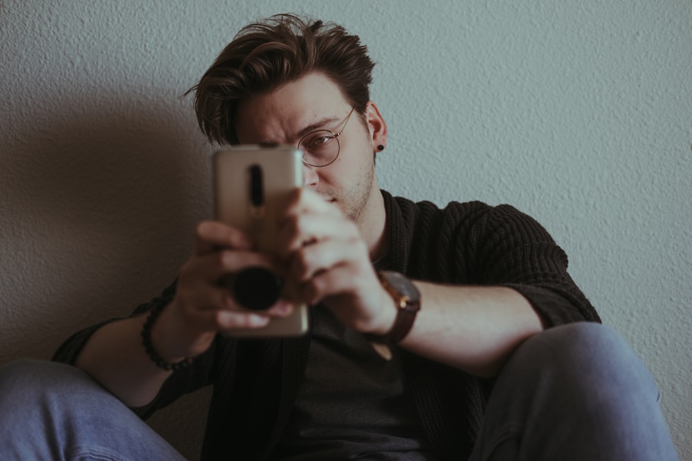 man in black crew neck shirt holding silver iphone 6