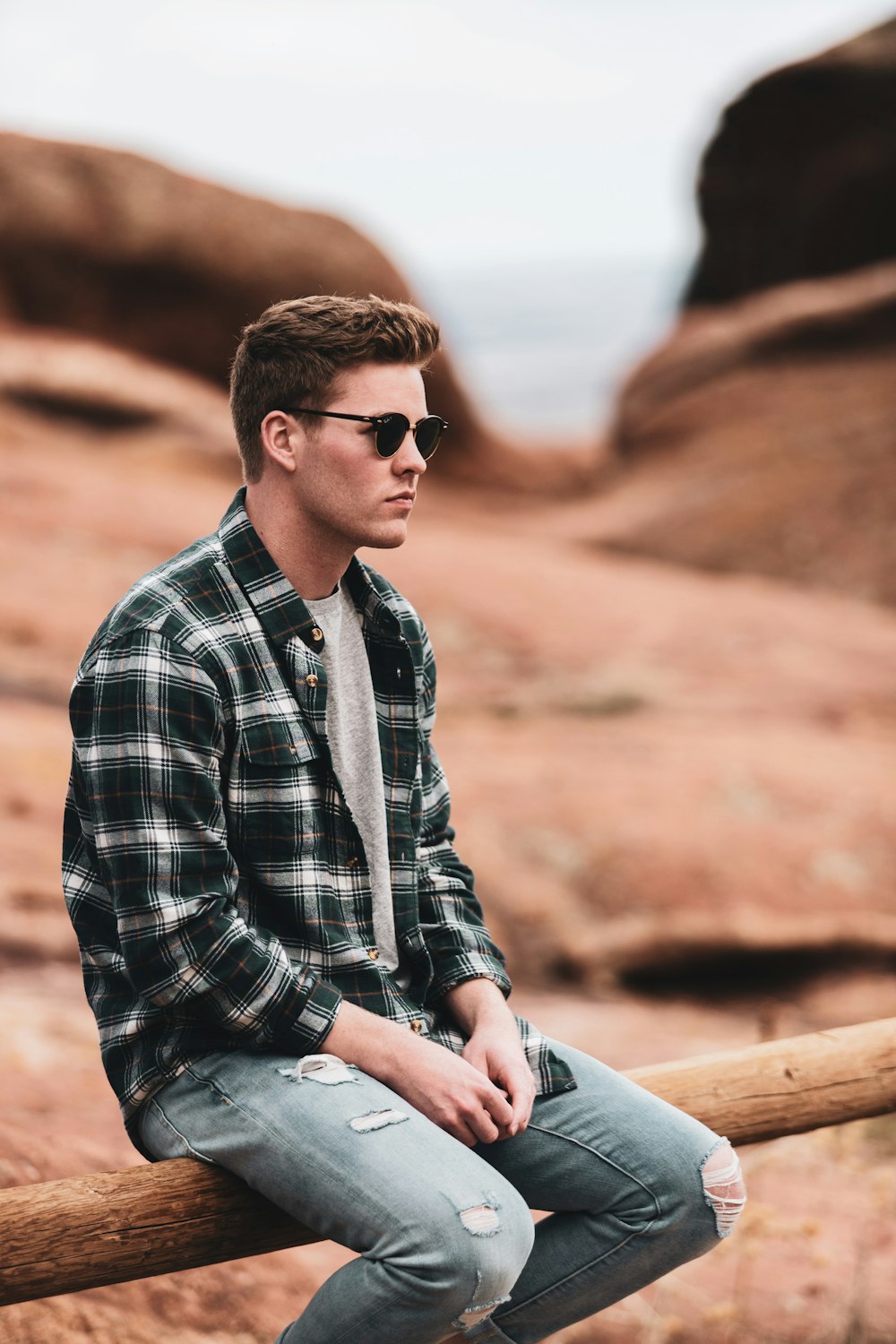 man in black and white plaid dress shirt wearing black sunglasses sitting on brown rock during
