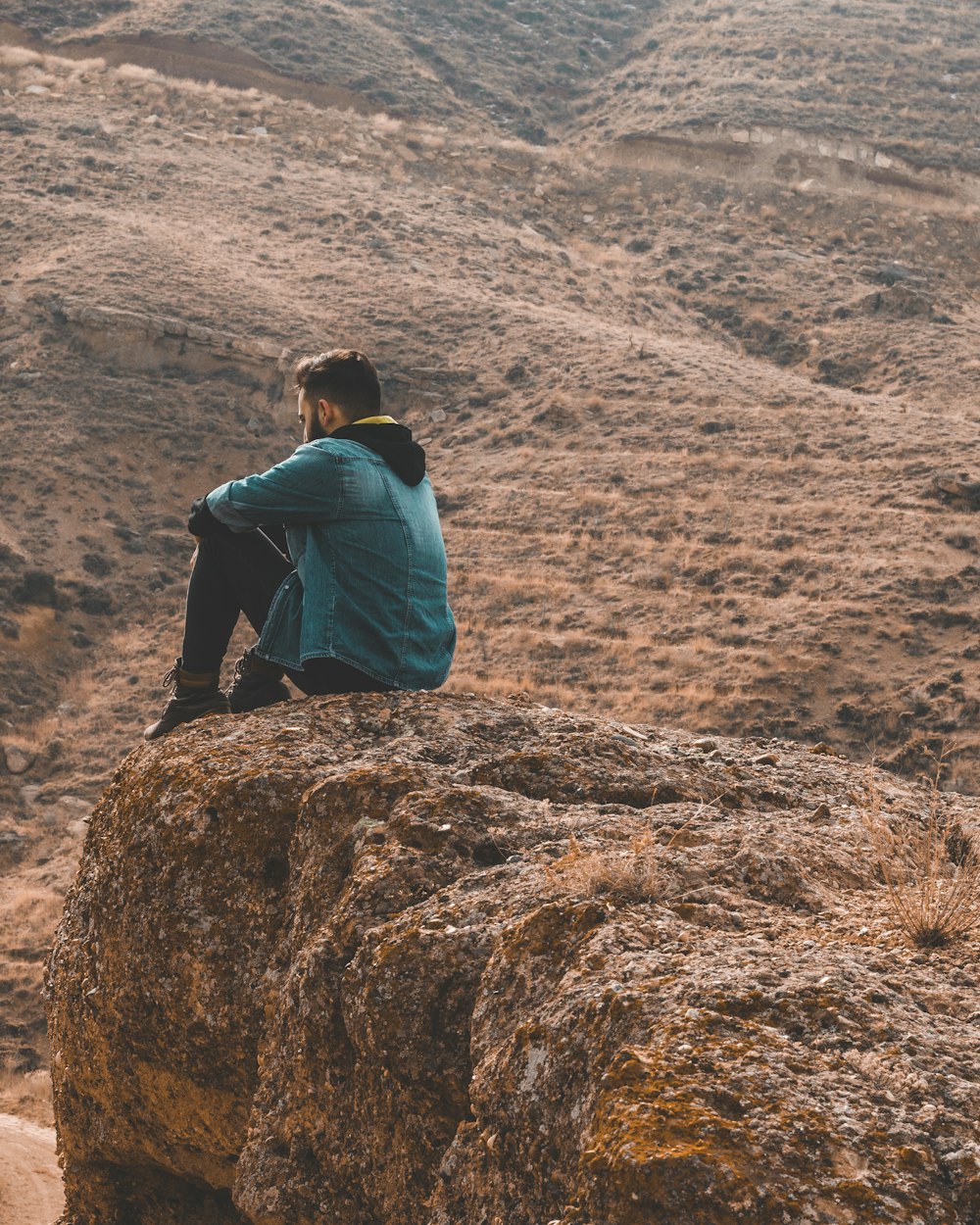 woman in blue jacket sitting on brown rock during daytime