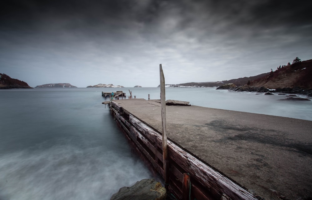 brown wooden dock on sea under white clouds during daytime