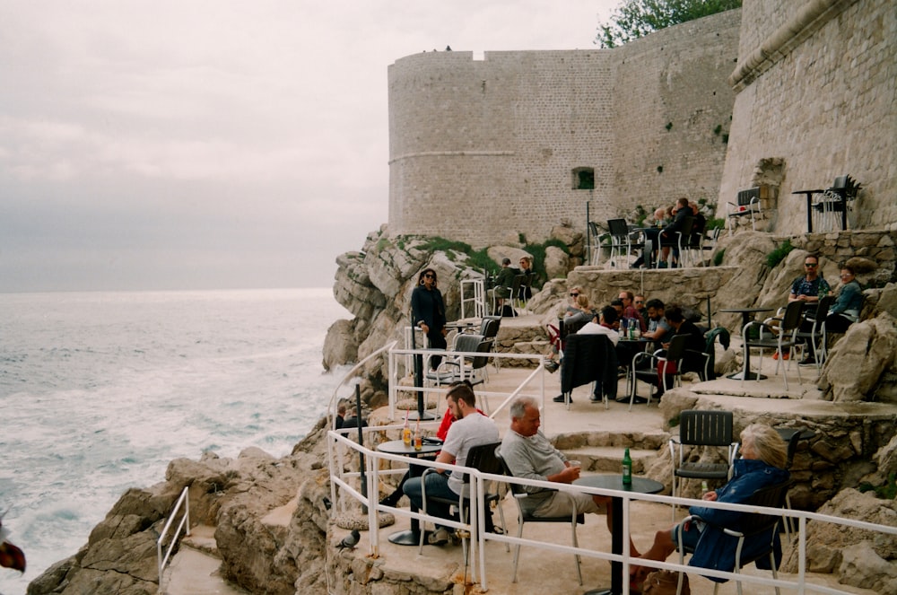 people sitting on white metal railings near body of water during daytime