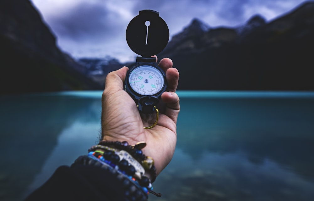 personne tenant une montre analogique ronde noire et argentée