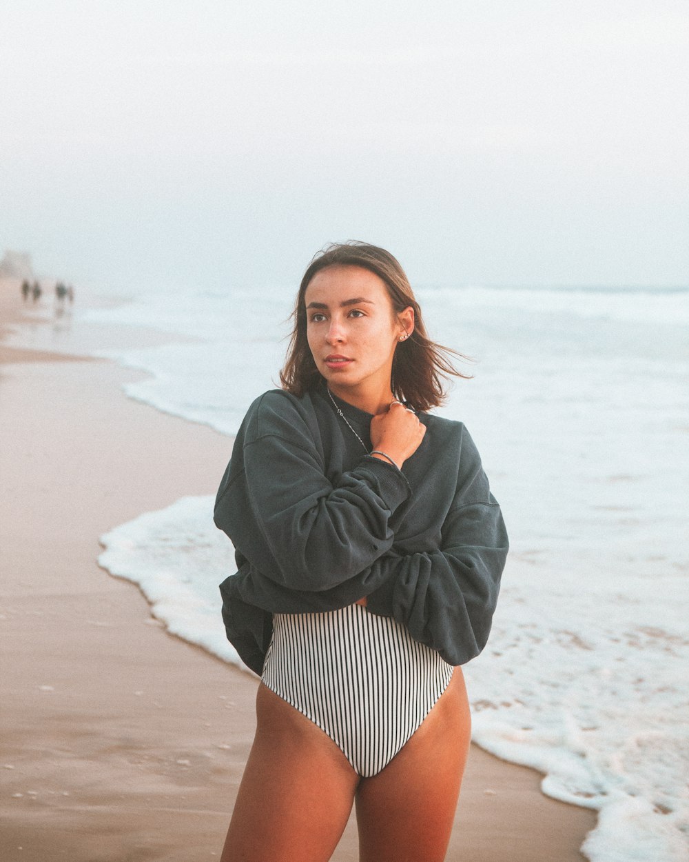 mulher na jaqueta preta e shorts de listras brancas e pretas em pé na praia durante o dia