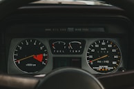 A detailed view of a car dashboard displaying various gauges, including a tachometer, fuel gauge, temperature gauge, and speedometer. The tachometer indicates engine speed in revolutions per minute, with a highlighted red zone. The fuel gauge shows fuel levels, and the temperature gauge reads engine temperature. The speedometer measures speed in kilometers per hour, showing vehicle mileage.