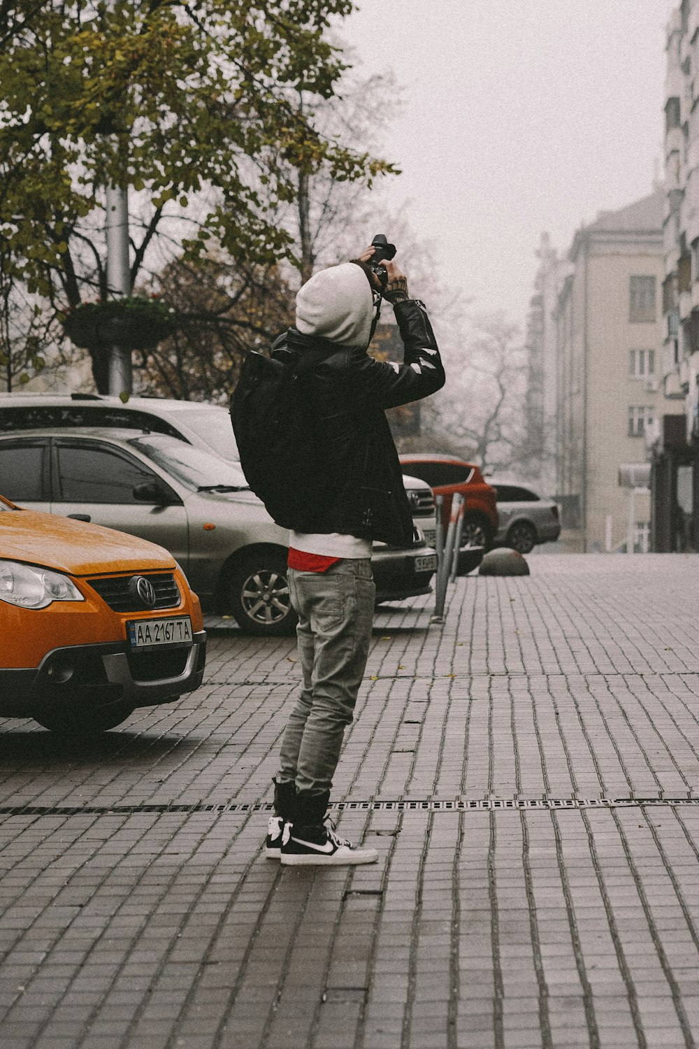 homem em jaqueta preta e calças cinzas tirando foto do carro laranja durante o dia