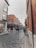 A bustling cobblestone street with people walking in different directions, flanked by buildings with brick facades. One building features American and Irish flags above a pub with decorative greenery. The sky is overcast, contributing to a subdued atmosphere.