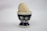 A wooden egg is placed in a decorative ceramic egg cup. The egg cup features a dark blue pattern with circular white and light brown designs resembling eyes or flowers. The background is a plain, light surface.
