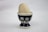 A wooden egg is placed in a decorative ceramic egg cup. The egg cup features a dark blue pattern with circular white and light brown designs resembling eyes or flowers. The background is a plain, light surface.