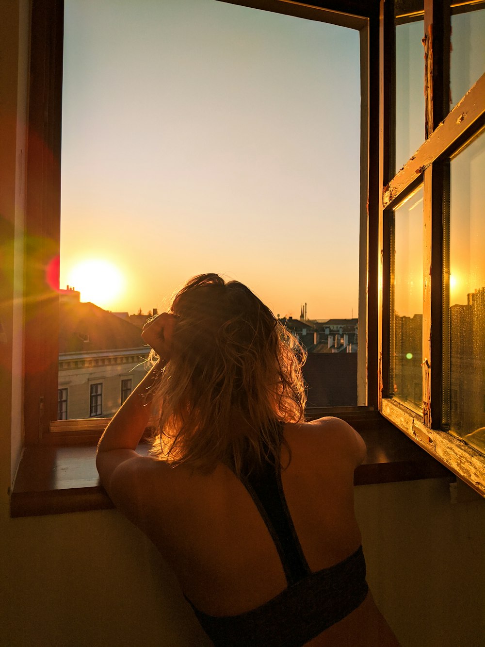 woman in black tank top sitting on brown wooden bench during sunset