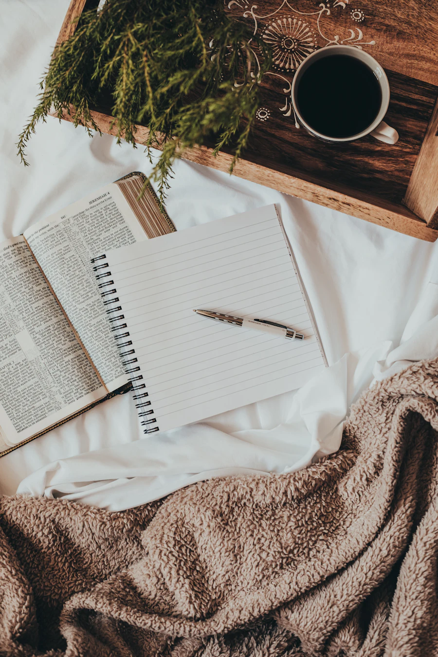 An open journal and pen on a wool blanket, beside a morning coffee.