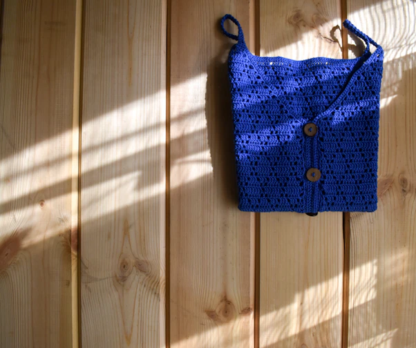 Brightly patterned crochet bags hanging on a vintage hook against a white wall.