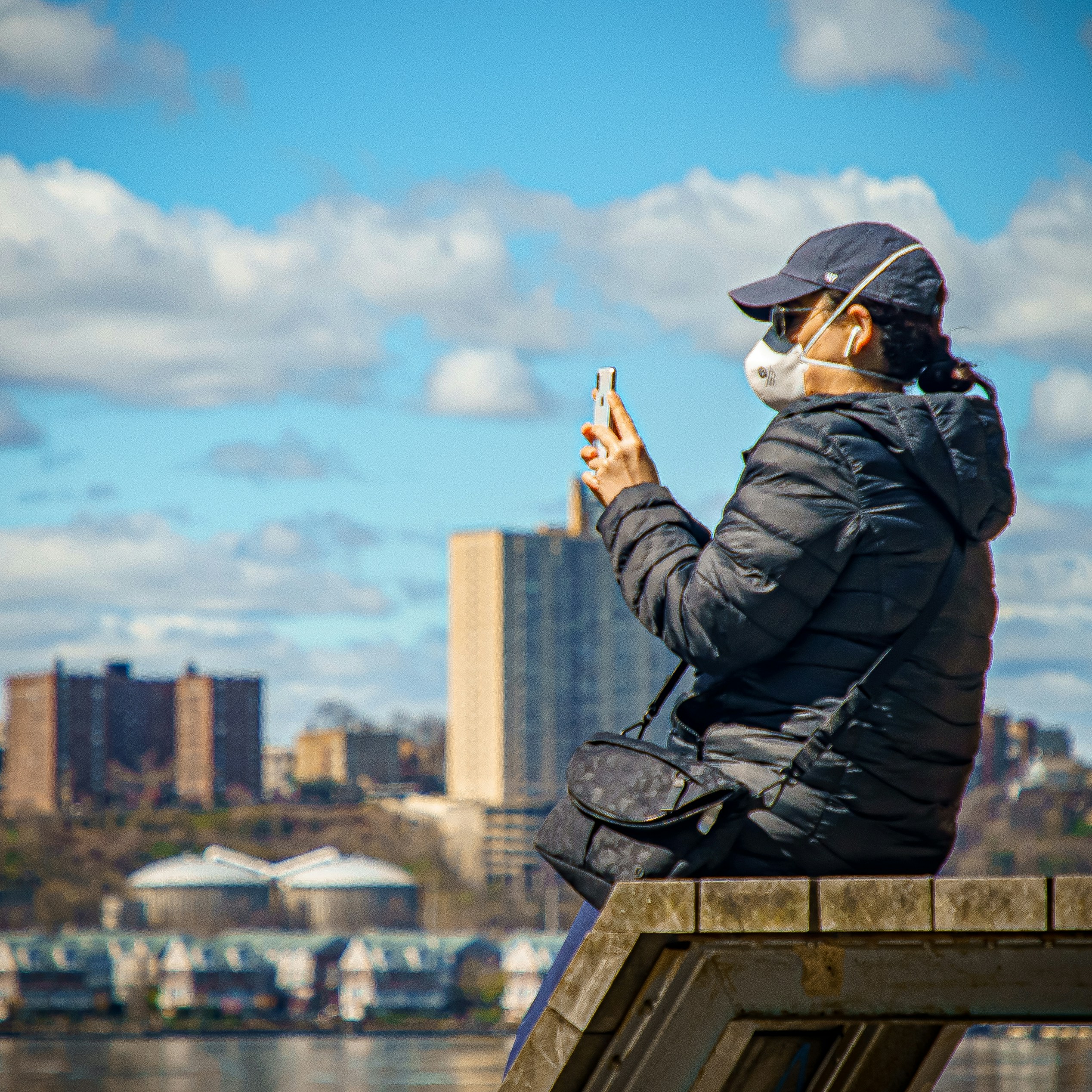 man in black leather jacket and black cap sitting on concrete wall during daytime