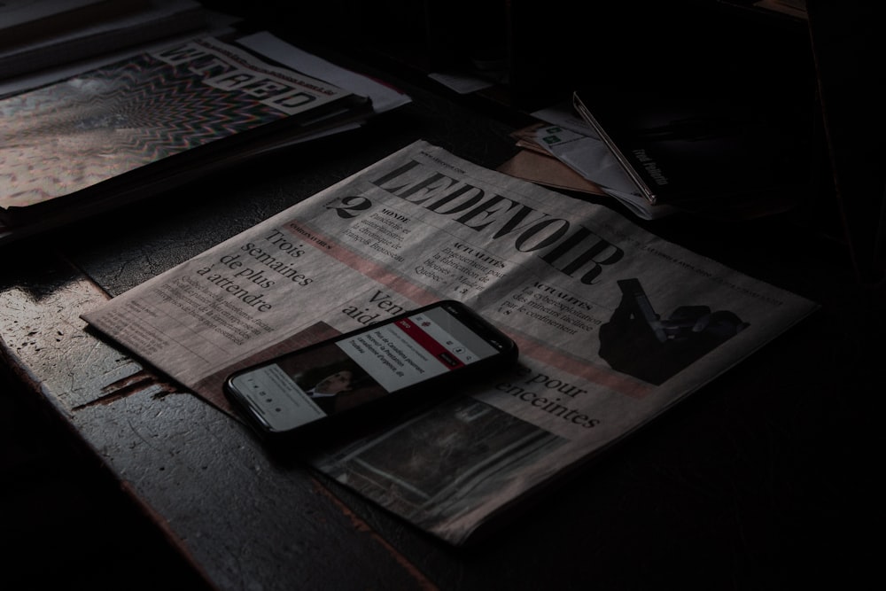 black smartphone on newspaper beside newspaper