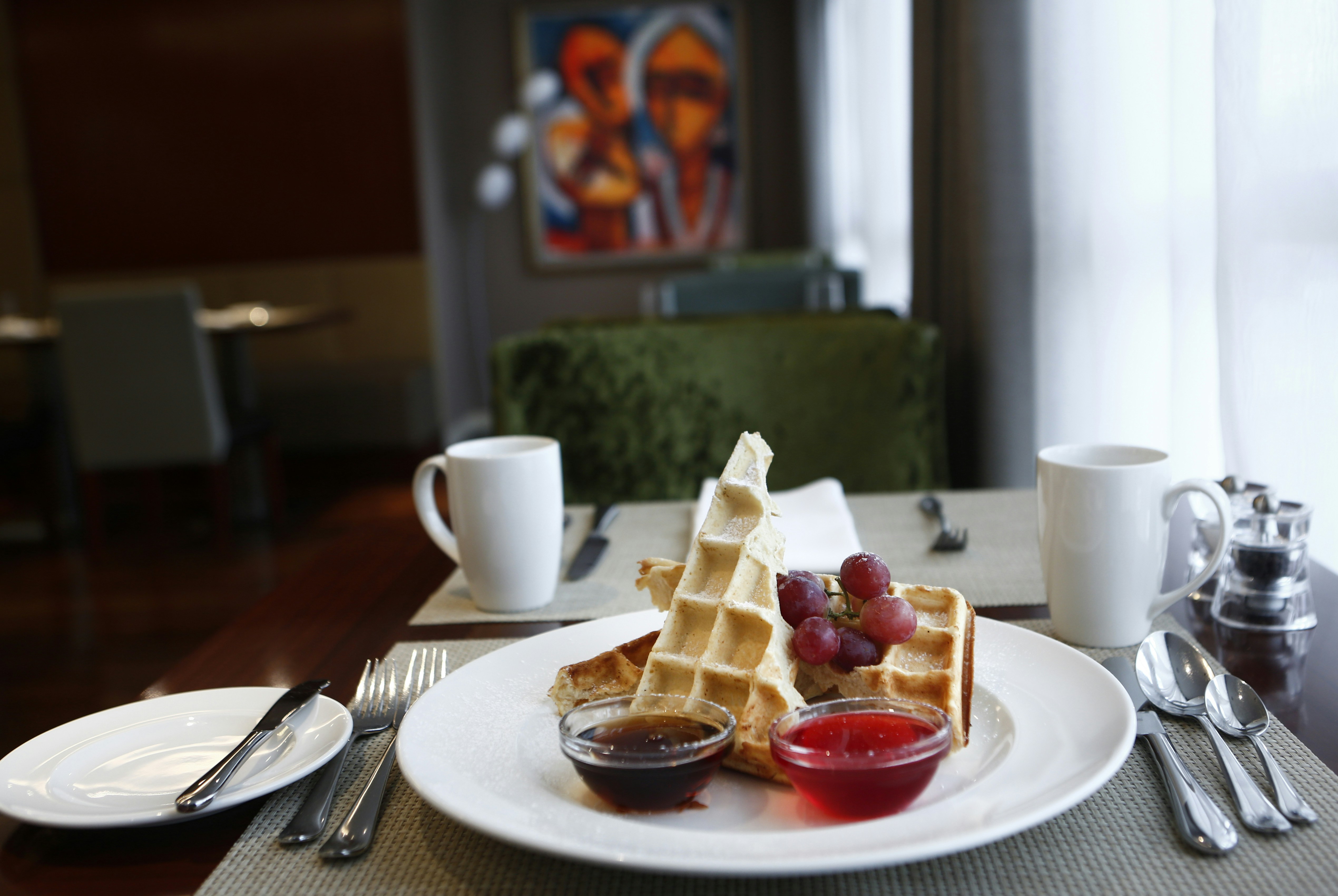 Waffle with strawberries and sauces on a white plate by a window