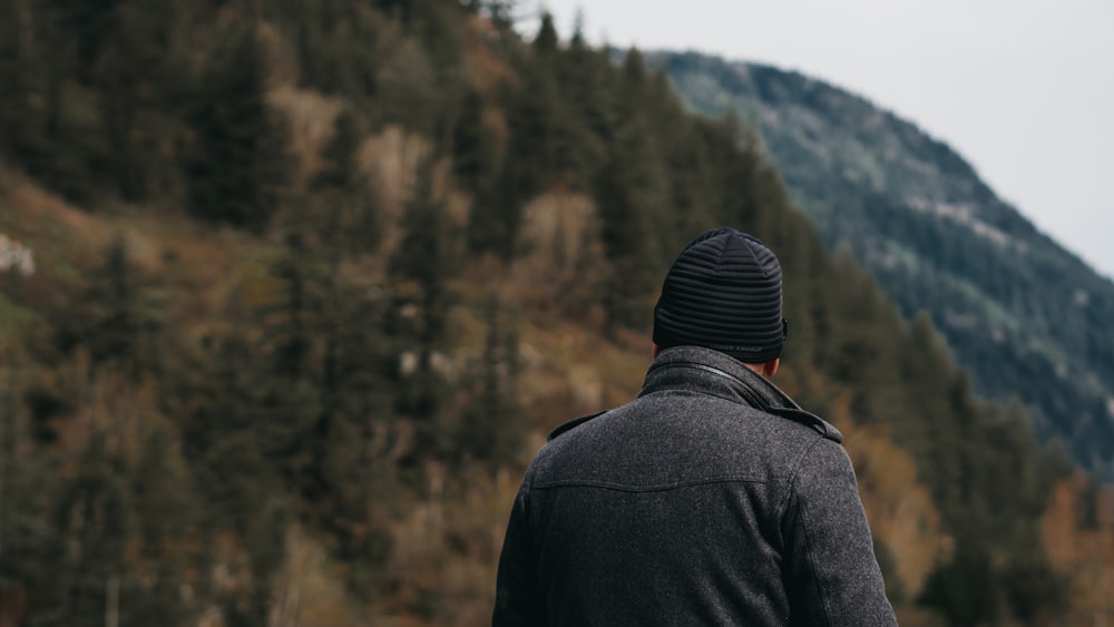 man in black jacket standing in front of green trees during daytime