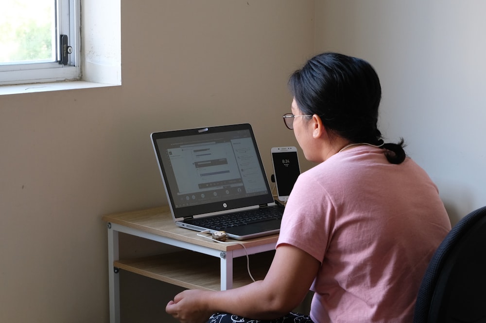 mulher na t-shirt cor-de-rosa que usa o computador portátil