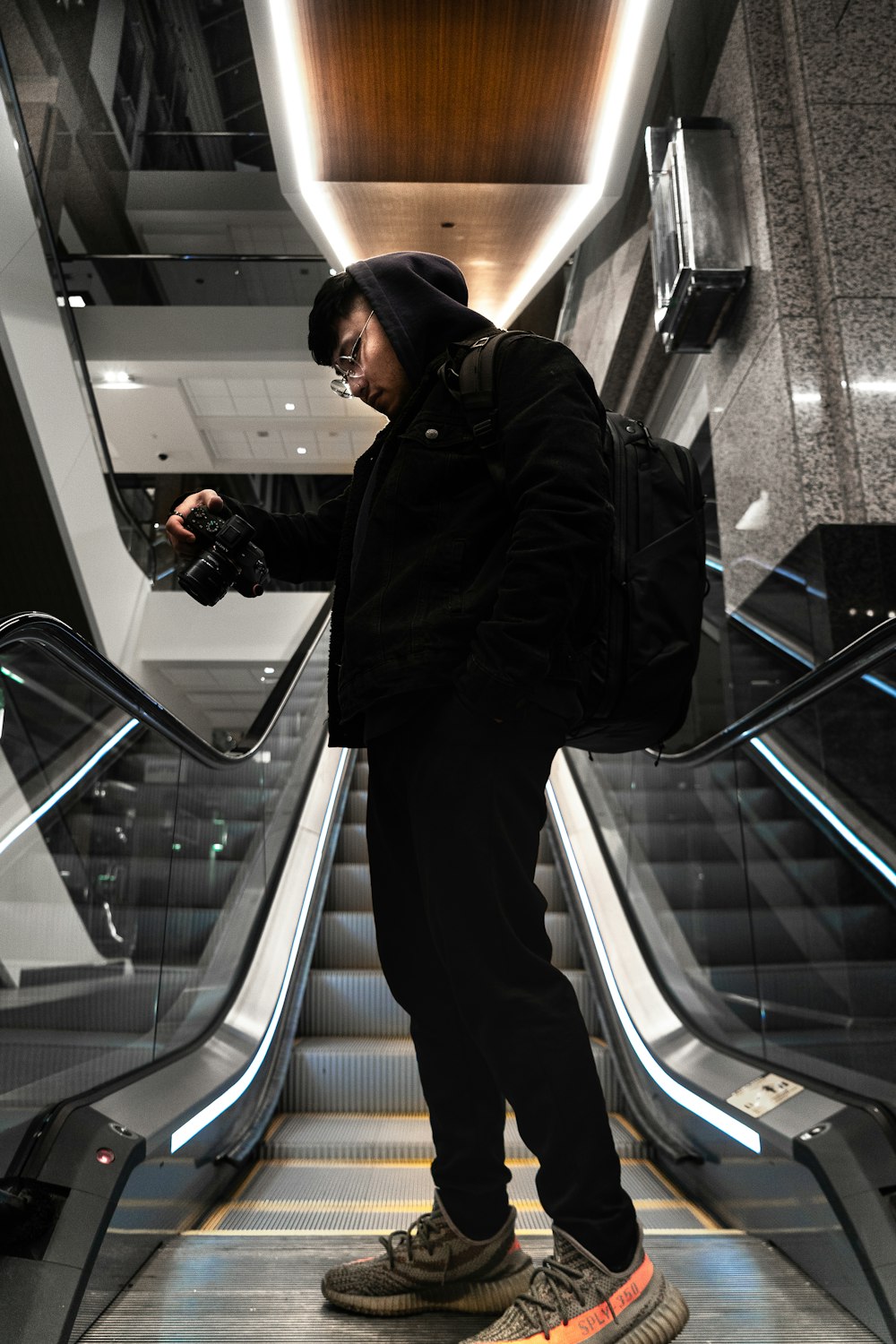 man in black jacket and black cap standing on escalator