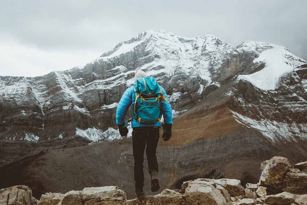 man in blue jacket and black pants standing on rock mountain during daytime