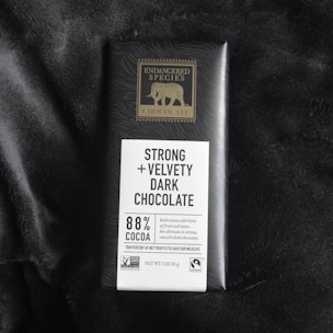 A bar of Endangered Species chocolate with packaging highlighting 'Strong + Velvety Dark Chocolate' containing 88% cocoa. The packaging features a gold elephant logo and mentions ethical sourcing certifications like Non-GMO Verified and Fairtrade.