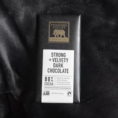 A bar of Endangered Species chocolate with packaging highlighting 'Strong + Velvety Dark Chocolate' containing 88% cocoa. The packaging features a gold elephant logo and mentions ethical sourcing certifications like Non-GMO Verified and Fairtrade.