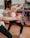 People are engaged in a fitness class, holding red dumbbells with both arms extended. The focus is on their arms and hands, with a blurred background showing a mirror and exercise balls. Participants are wearing athletic attire.