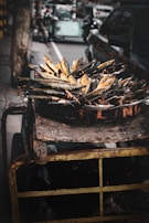 A cart filled with grilled or smoked fish is positioned on a street, with several vehicles and urban elements visible in the background. The fish are arranged closely together on a large metallic tray, displaying a rustic and urban market atmosphere. The cart appears weathered, enhancing the gritty street vibe.