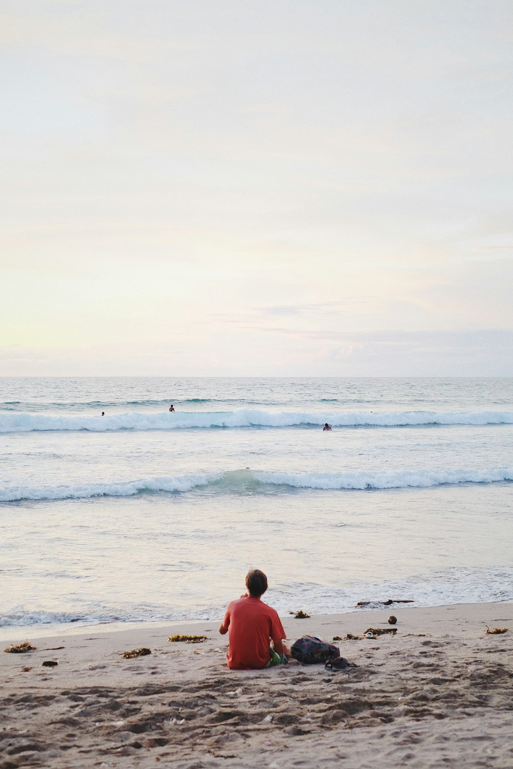 man in red shirt sitting on beach during daytime