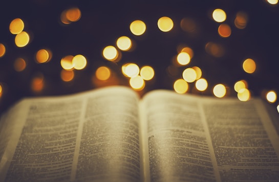 An open book with visible text set against a background of blurred, warm glowing lights, suggesting a soft and cozy atmosphere.