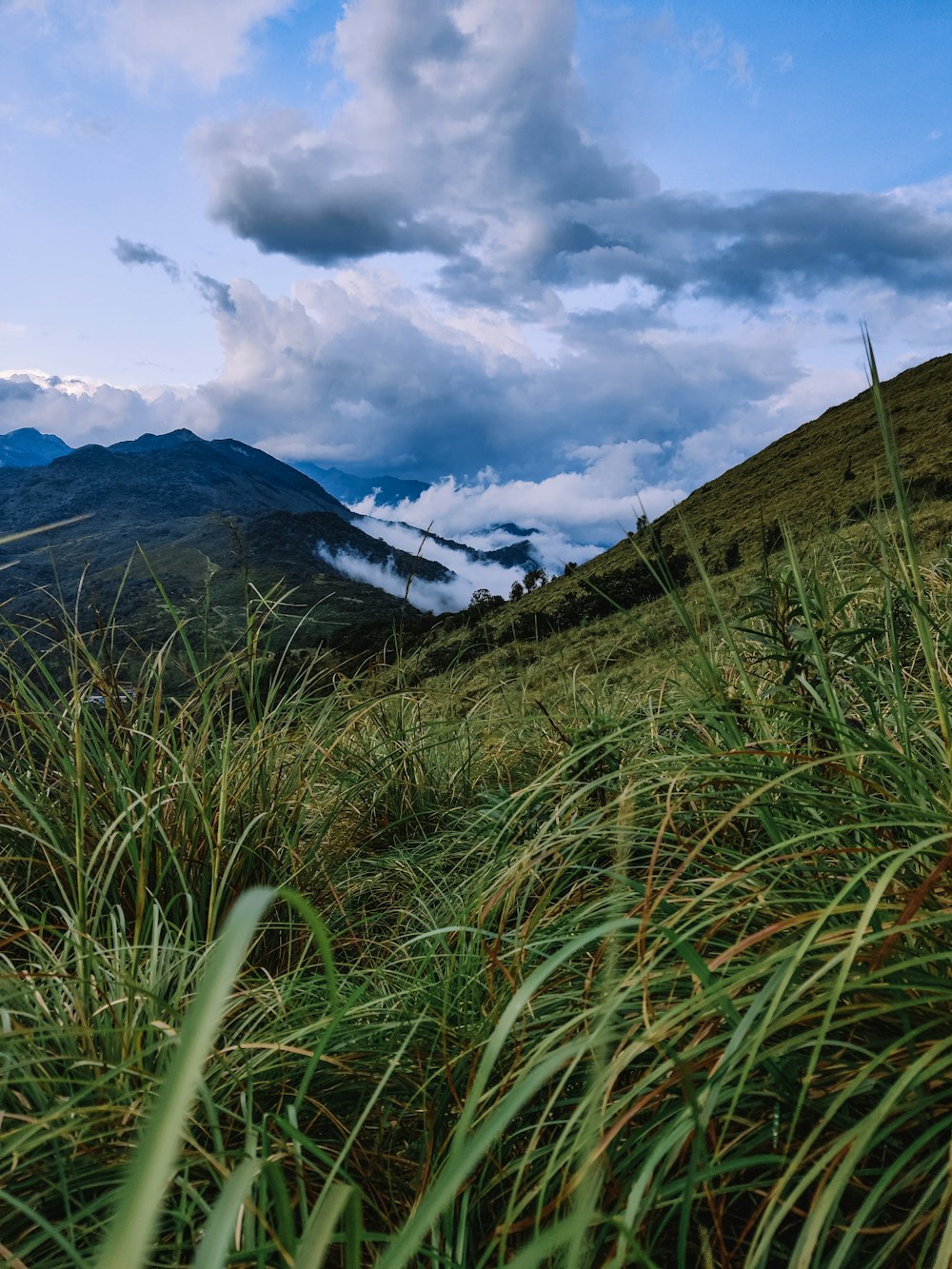 green grass field near mountain under white clouds during daytime