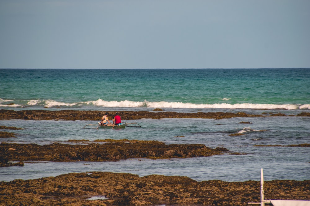 person in red shirt sitting on rock by the sea during daytime