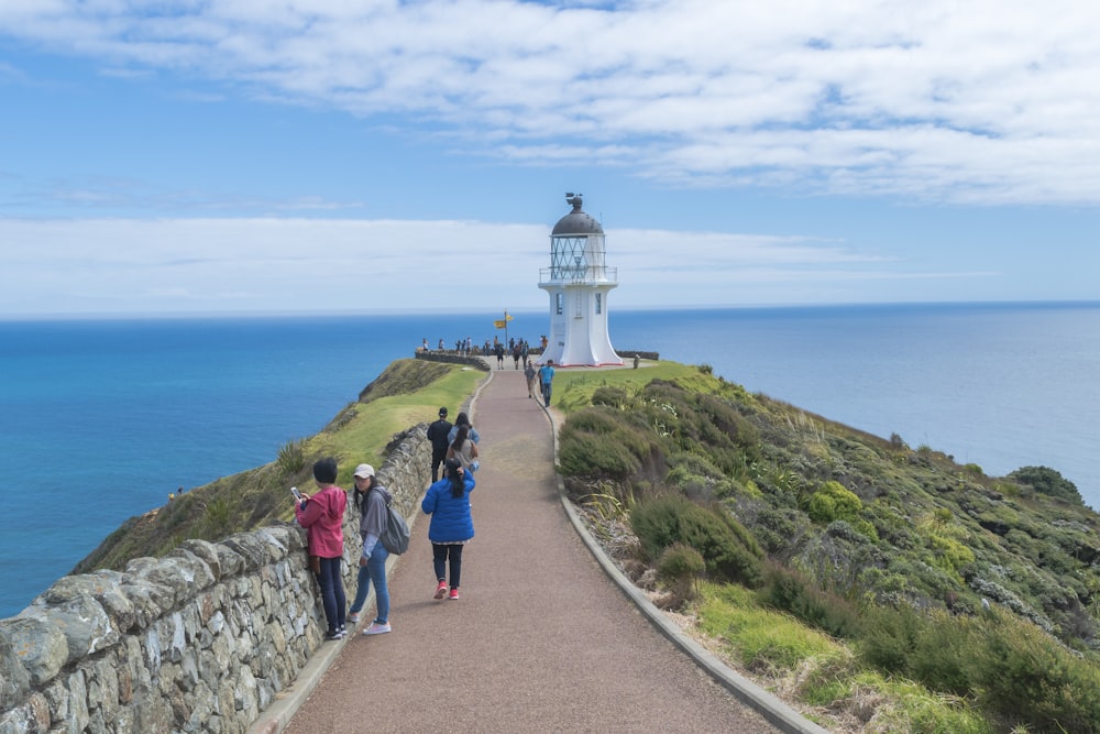 pessoas andando no caminho perto do farol sob o céu azul durante o dia