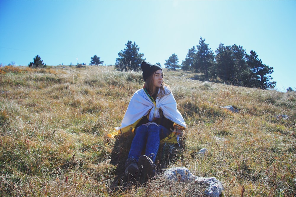 Femme en robe verte et jaune assise sur le champ d’herbe brune pendant la journée