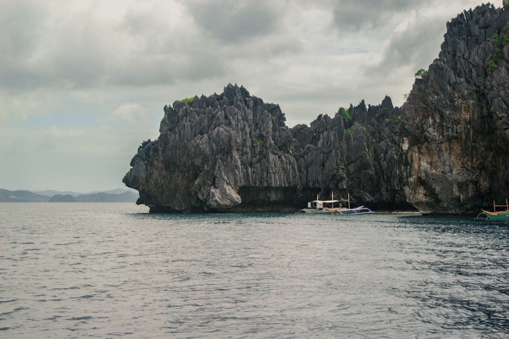 white boat on sea near green and brown rock formation under white clouds during daytime