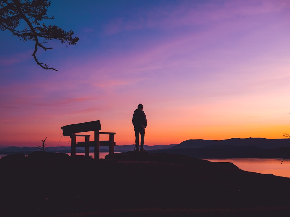 silhouette of man standing on brown wooden bench during sunset