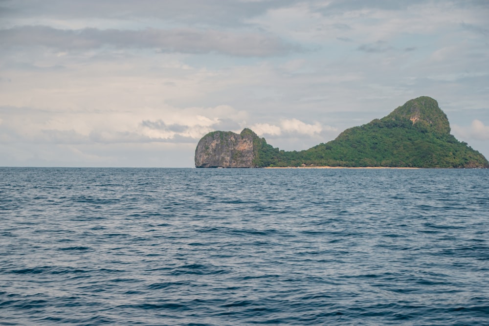 green and brown rock formation on sea under white clouds during daytime