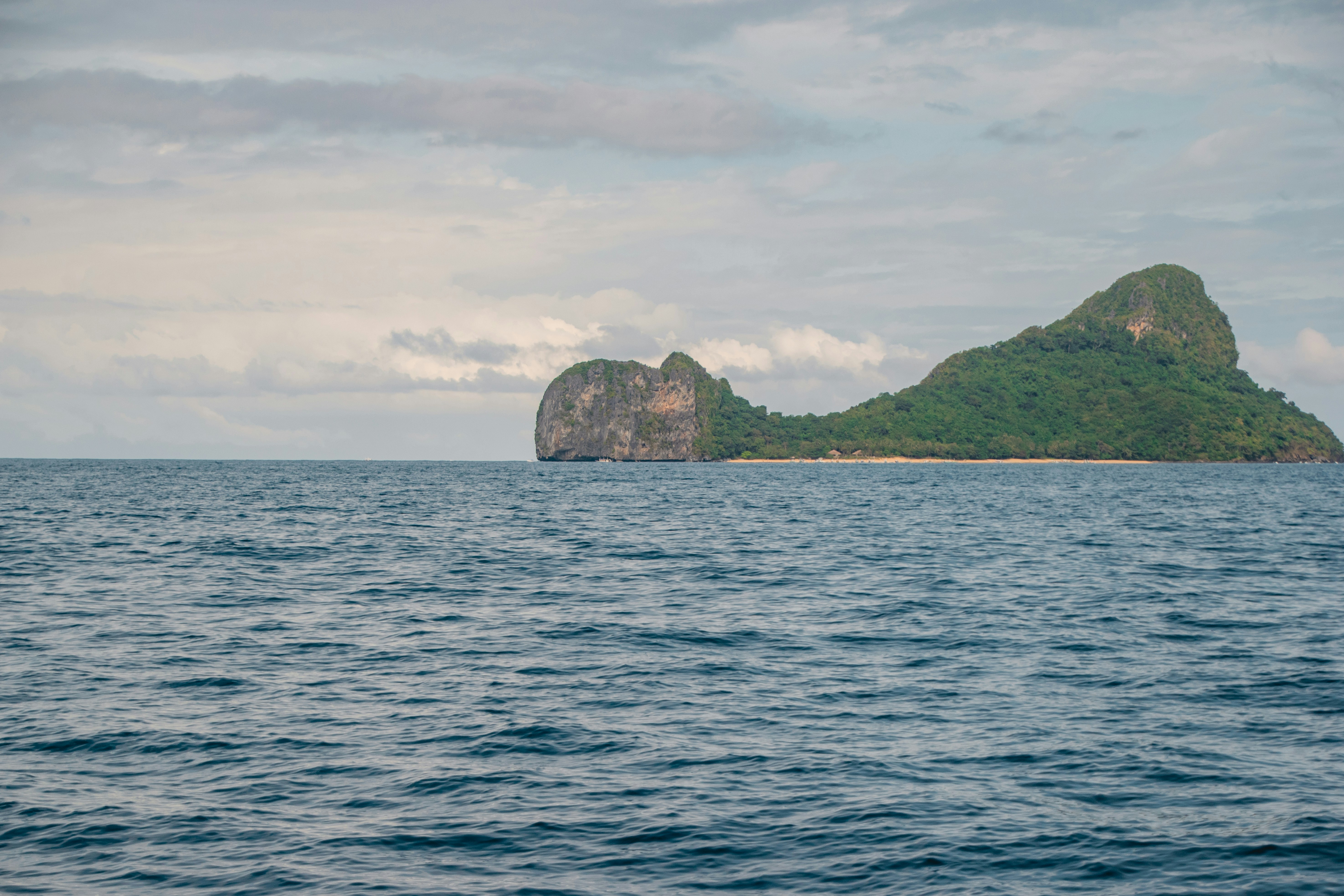 green and brown rock formation on sea under white clouds during daytime