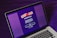 A laptop displays a screen with a vibrant purple background featuring the text 'Wash & Vax' with stylized virus iconography above it. Detailed text below outlines a call to action related to vaccines and social distancing, with a prominent 'start' button visible.