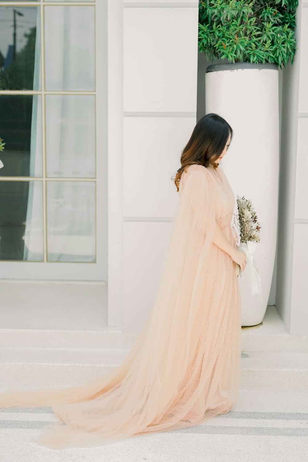 a woman in a long dress standing next to a plant