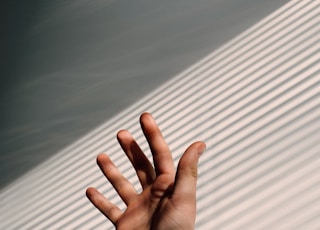 persons left hand on white window blinds