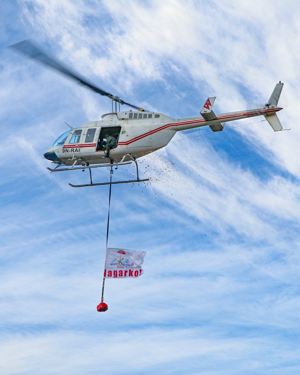 昼間の青空の下を飛ぶ白と赤のヘリコプター