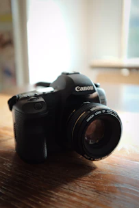 Close-up of a sleek modern DSLR camera resting on a wooden table with soft natural light highlighting its details.