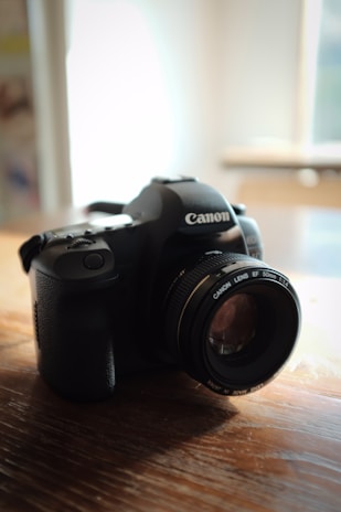 A sleek black DSLR camera resting on a wooden table with natural light highlighting its lens.