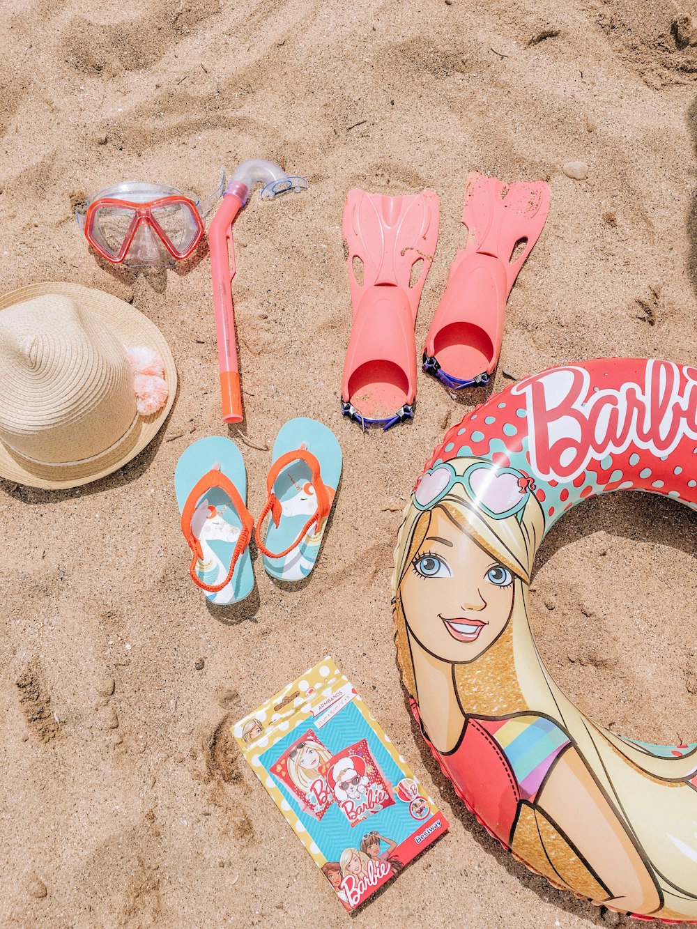 Tongs rouges et bleues à côté d’un chapeau de soleil marron sur le sable