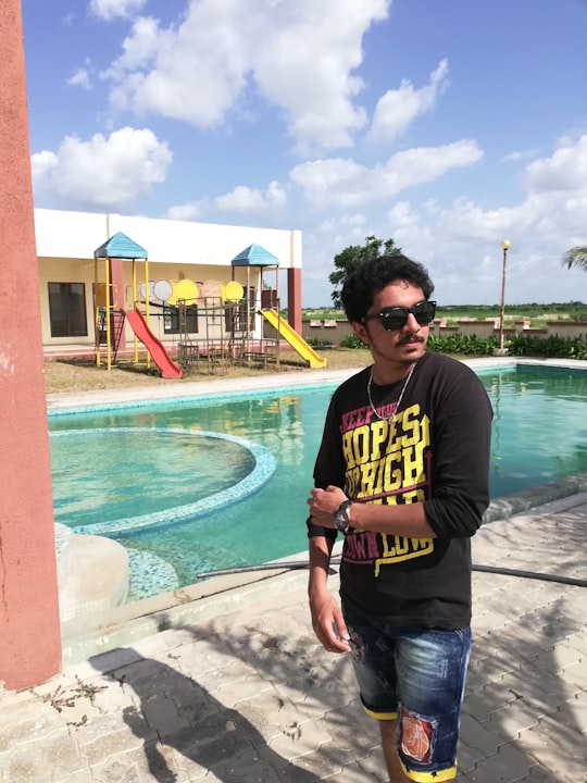 man in black and yellow crew neck t-shirt standing beside swimming pool during daytime in Rajkot India