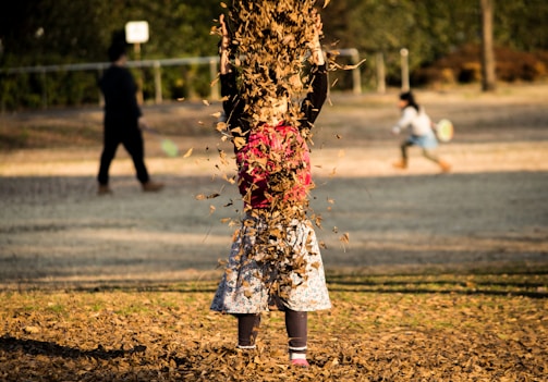 A whimsical outdoor scene with children playing among autumn leaves, dressed in vibrant fashion.