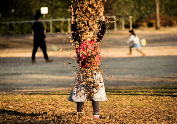 A happy child in a colorful outfit running through a sunlit park with autumn leaves.